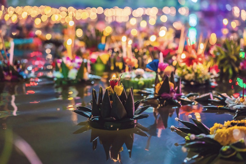 Le Krathong lumineux orné de fleurs et de bougies flottant sur l''eau.